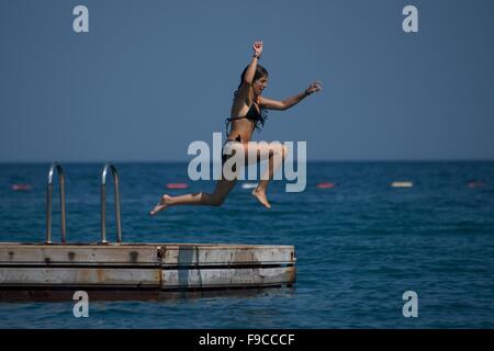 Ragazza in Bikini nero saltando in acqua Foto Stock