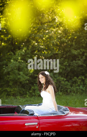 Bella bruna sposa su un verde prato con auto rétro Foto Stock