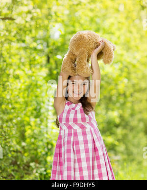 Carino bambina in abito rosa è la riproduzione di marrone con Teddy nel verde della natura Foto Stock