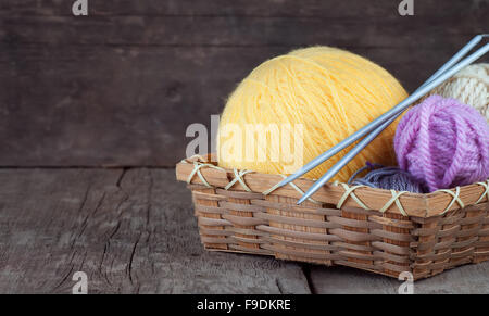 Palline di filato nel cestello con aghi di tessitura su sfondo di legno Foto Stock