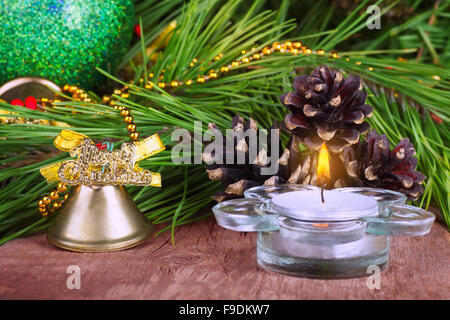 Decorazione di Natale candela che brucia il ramo di abete e coni con campana dorata e luminosa sfera su sfondo di legno Foto Stock