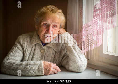 Una donna anziana si siede da solo vicino alla finestra. Foto Stock