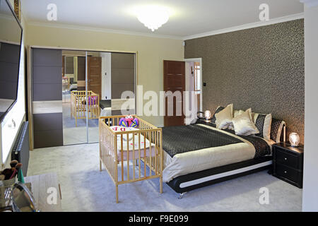 Un recentemente decorate in maniera moderna camera da letto con un letto doppio e la culla per bambini in contrasto con i mobili di tendenza Foto Stock