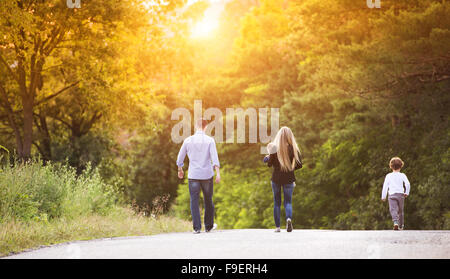 Felice famiglia giovane a piedi giù per la strada al di fuori nel verde della natura. Foto Stock