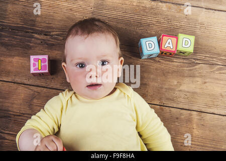 Little baby con cubetti con papà segno su sfondo di legno Foto Stock