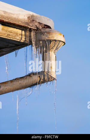 Ghiaccioli ghiaccio sull'angolo del tetto in corrispondenza della bocca drainpipe Foto Stock