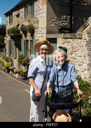 Regno Unito, Inghilterra, Derbyshire, Hartington, Church Street, madre anziana utilizzando walker con figlia senior Foto Stock