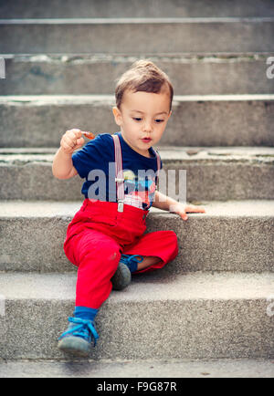 Carino piccolo ragazzo seduto sulle scale durante un giorno di estate Foto Stock