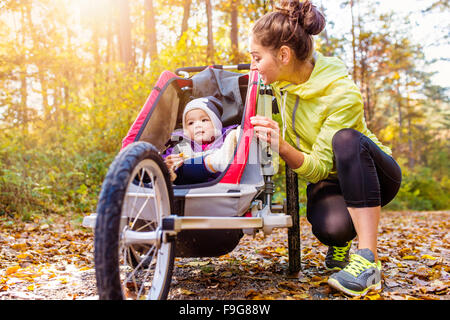 Giovane e bella madre con sua figlia in jogging passeggino in esecuzione al di fuori in autunno la natura Foto Stock