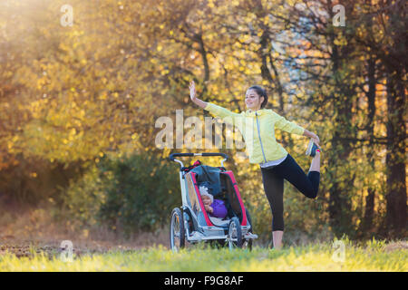 Giovane e bella madre con sua figlia in jogging passeggino in esecuzione al di fuori in autunno la natura Foto Stock