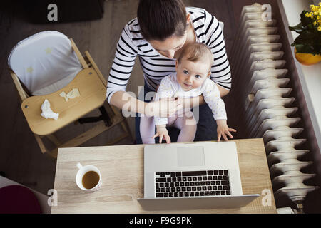 Giovane madre in home office con computer e sua figlia Foto Stock