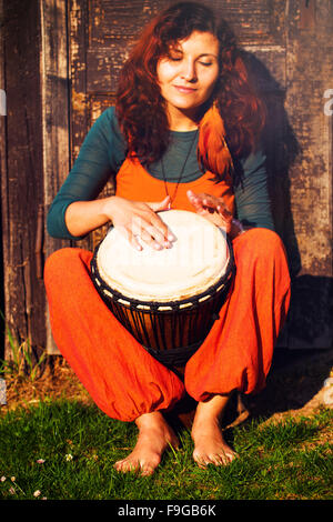 I giovani scalzi lady batterista giocando sul suo djembe sul tamburo in legno rustico sfondo della porta. Foto Stock