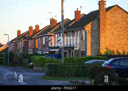 Case Hedgerows automobili parcheggiate marciapiedi e lampioni sera ombre lunghe e bagliore rosso contro l'arancione rosso mattone lavoro. Foto Stock