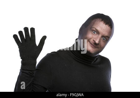 Ladro di balaclava facendo facce buffe, vestito di nero. Studio shot su sfondo bianco. Foto Stock