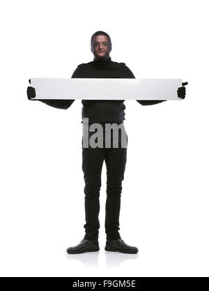 Ladro con passamontagna sul suo volto, vestita di nero, tenendo un banner di vuoto. Studio shot su sfondo bianco. Foto Stock