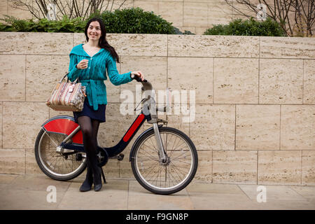 Giovane donna con una bici a noleggio in strada Foto Stock