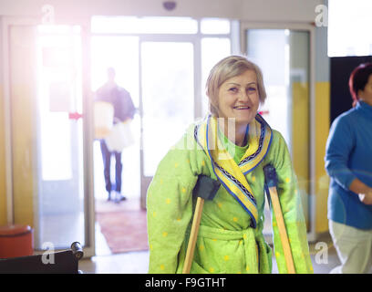 Senior donna feriti a piedi attraverso il corridoio di ospedale con le stampelle Foto Stock