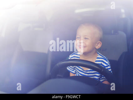 Little Boy giocando con un volante in un auto Foto Stock