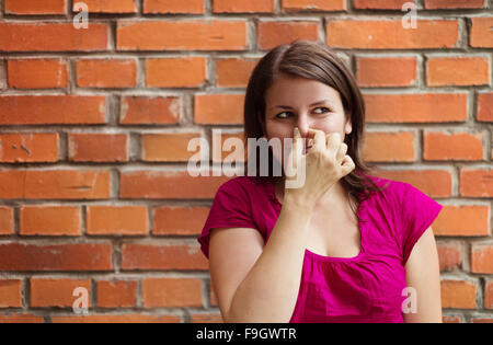 Bella giovane donna fare facce buffe su un muro di mattoni in background Foto Stock