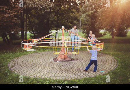 La famiglia felice al di fuori in un parco su una vecchia giostra. Foto Stock