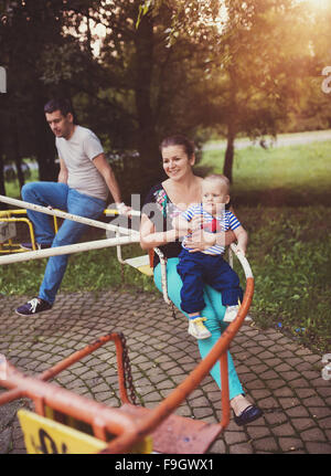 La famiglia felice al di fuori in un parco su una vecchia giostra. Foto Stock