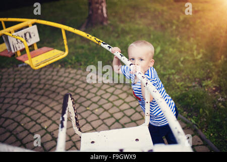 Carino piccolo ragazzo in un parco su una vecchia giostra. Foto Stock