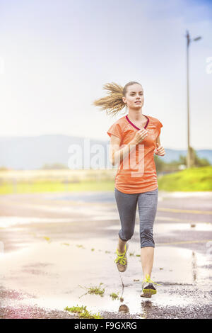 Giovane donna jogging su asfalto in condizioni di tempo piovoso Foto Stock