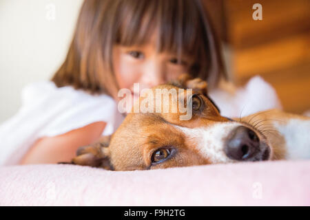 Il Toddler ragazza e il suo cane la posa sul letto Foto Stock