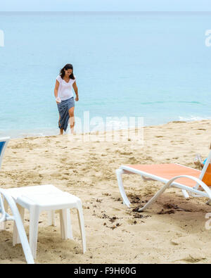 Un pelo scuro donna caucasici in una gonna lunga passeggiate fino dall'acqua sulla spiaggia a St. Croix, U.S. Isole Vergini. Foto Stock