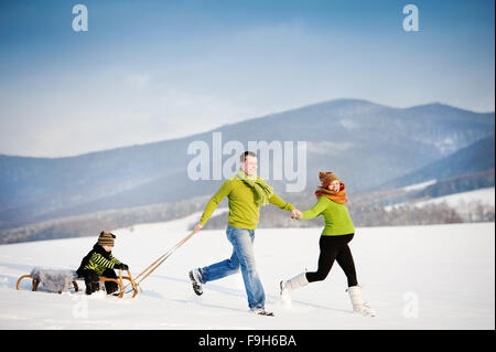 Genitori felici con il loro figlio equitazione sulla slitta avendo divertimento fuori nella neve. Foto Stock