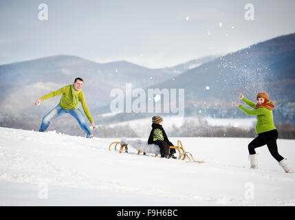 Genitori felici con il loro figlio equitazione sulla slitta avendo divertimento fuori nella neve. Foto Stock