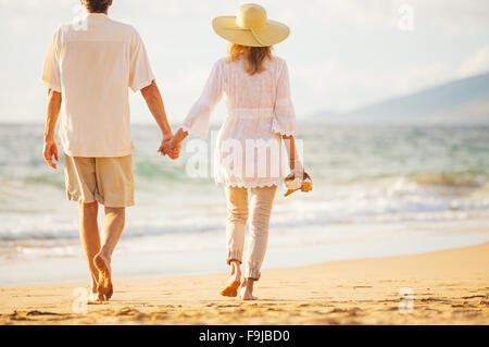 Romantica felice coppia di mezza età godendo bel tramonto a piedi sulla spiaggia tenendo le mani Foto Stock