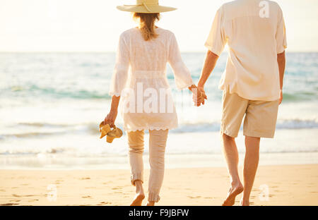 Romantica felice coppia di mezza età godendo bel tramonto a piedi sulla spiaggia tenendo le mani Foto Stock