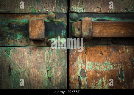 Extreme close-up di un chiavistello arrugginito, montato su una vecchia porta di legno con pareti scrostate. Foto Stock
