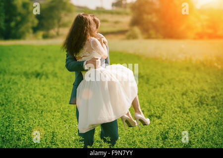 Felice kissing sposi all'aperto sul prato. L uomo è in possesso di una donna nelle sue braccia Foto Stock