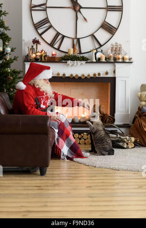 Santa Claus Warming alimentando il suo gatto di casa Foto Stock