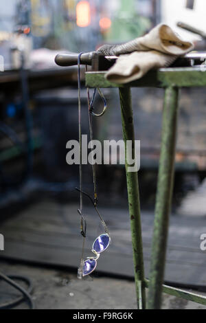 Guanti e occhiali protettivi su un banco di lavoro ad una soffiatura del vetro Fabbricazione / forno per vetro. Foto Stock