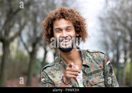 Ritratto di uomo sorridente con tinti boccoli indossando camouflage shirt puntando sul visore Foto Stock
