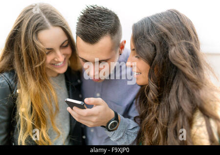 Tre amici guardando il telefono cellulare insieme Foto Stock
