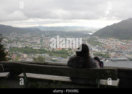 Una donna seduta su una panchina guardando giù su Bergen dal Monte Floyen in Norvegia Foto Stock