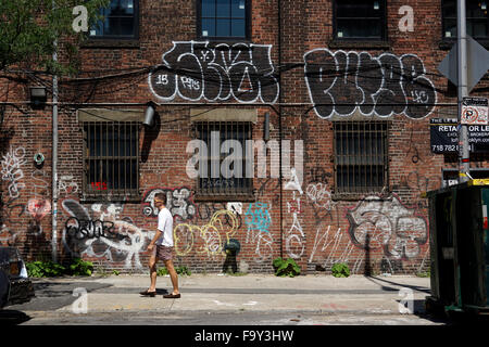 Un uomo che cammina da una coperta di graffiti parete edilizia di Williamsburg. Brooklyn. New York, Stati Uniti d'America Foto Stock