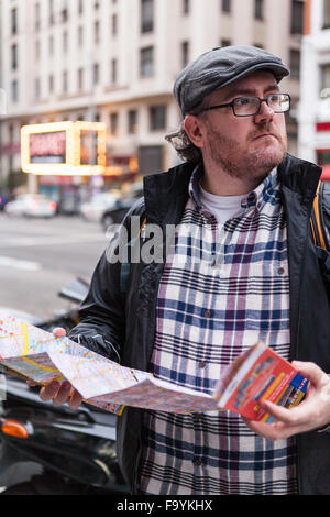 Giovane viaggiatore uomo con gli occhiali e un cappello in cerca di un posto in una mappa Foto Stock