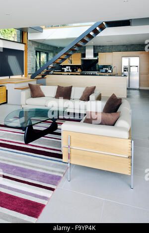 Gli spazi interni di una casa moderna sulla scogliera che si affaccia sul mare. Grandi pannelli di vetro e pareti e ripiani in legno e divisori in camera. Area soggiorno. Scala di flottante. Foto Stock
