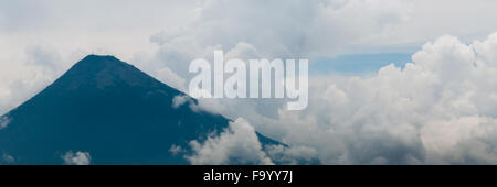 Grande cima del vulcano circondato dalla nebbia e dense nubi su campo verde Foto Stock