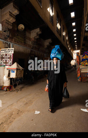 Tradizionale egiziana donna vestita di nero abaya portante, bilanciamento del sacchetto pieno sulla sua testa attraverso l'Al Khiamiyya bazaar Foto Stock