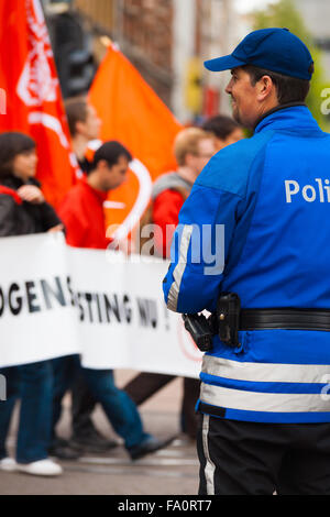 Alle spalle di vista di gentile, gioviale, ridendo poliziotto fiamminga sorridente, guardando oltre dimostranti portando bandiere, striscioni al giorno di maggio Foto Stock