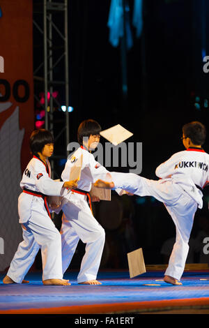 Taekwondo ragazzo coreano di calci e la rottura di due assi di legno tenuto dai colleghi in un libero esterno notte le prestazioni nelle vicinanze city hal Foto Stock