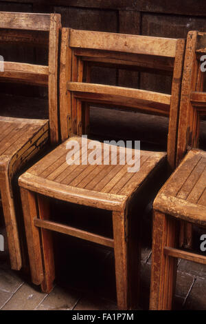 Vintage verticale di legno sedie impilati e disposti in fila contro in pannelli di legno parete Foto Stock