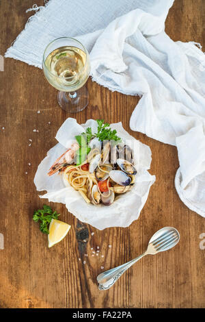 Piatti di pasta. Linguine con vongole e gamberetti in ciotola, bicchiere di vino bianco su legno rustico sfondo, vista dall'alto