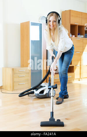 Con i capelli lunghi donna in cuffia la pulizia con aspirapolvere sul pavimento in parquet a casa Foto Stock